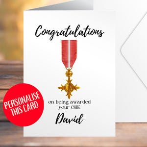 Puede incluir: Tarjeta de felicitación blanca con la palabra "Congratulations" en cursiva. La tarjeta presenta una medalla dorada y roja, con el texto "on being awarded your OBE" y el nombre "David". Un círculo rojo con el texto "Personalise this card" está en la parte inferior izquierda.