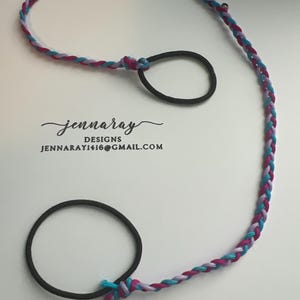 May include: A braided cord with purple, teal, and pink strands, tied to two black hair elastics.