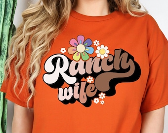 May include: Orange t-shirt with the text "Ranch Wife" in a retro font with colorful flowers.