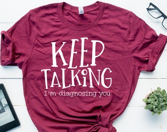 Könnte beinhalten: Ein maroonfarbenes T-Shirt mit dem Text "KEEP TALKING I'm diagnosing you" in Weiß.