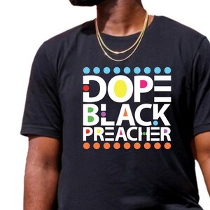 May include: A black t-shirt with a colorful graphic design that says "Dope Black Preacher".