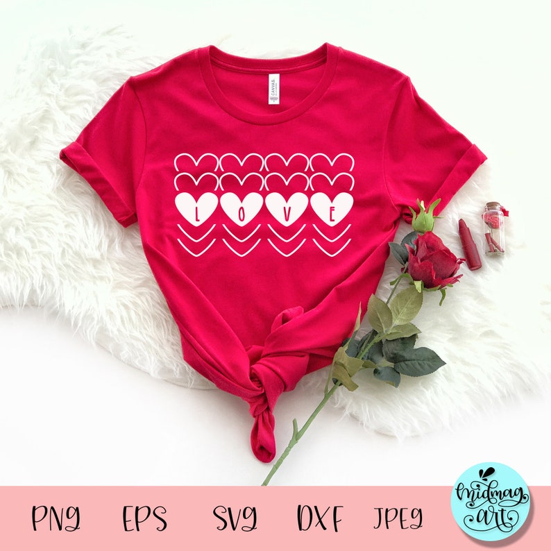 May include: A red t-shirt with the word "LOVE" in white, designed with heart shapes. The shirt is knotted at the bottom. A red rose, lipstick, and a small glass jar with red items are placed near the shirt.