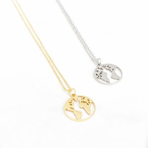 Puede incluir: Dos collares con colgantes de globo terráqueo. Uno es dorado, el otro plateado. Cada colgante presenta un diseño recortado de los continentes de la Tierra. Los collares tienen cadenas delicadas y se muestran sobre un fondo blanco.