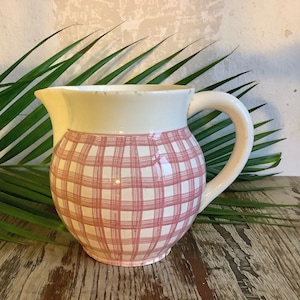 Peut inclure: Un pichet en céramique blanche avec un motif à carreaux rose et blanc. Le pichet a une anse et un corps arrondi.