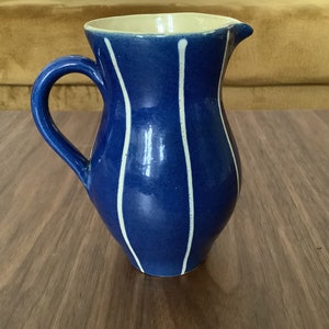 Può includere: Un'anfora in ceramica blu con strisce bianche. L'anfora ha un corpo arrotondato e un manico.