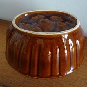 Könnte beinhalten: Eine braune Keramik-Backform mit geriffeltem Design. Die Form hat einen weißen Rand und eine leicht erhöhte Mitte.