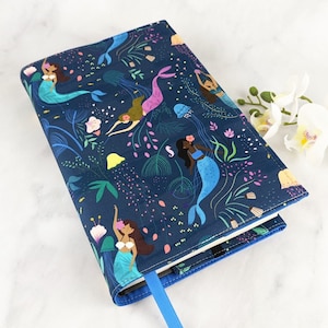May include: A blue book cover with a colorful pattern of mermaids, seahorses, and jellyfish. The cover is made of fabric and has a blue ribbon bookmark.