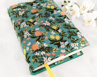 Puede incluir: Una cubierta de libro de color turquesa con un patrón floral que presenta flores blancas, hojas verdes y cítricos amarillos y naranjas.