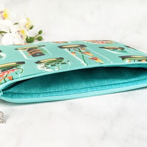 Puede incluir: Una bolsa de cremallera de color turquesa con un estampado floral que presenta frascos de plantas y hongos. La bolsa est&aacute; abierta y el forro es de color turquesa claro.