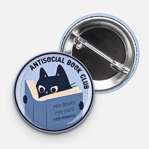 May include: A light blue button pin with the text "Antisocial Book Club" encircling a black cat reading a blue book. The book reads "Pro Books, Pro Cats, Pro People."