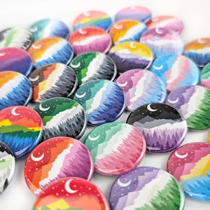 May include: A collection of colorful round buttons with landscape designs. Each button features a mountain scene with trees, a crescent moon, and a gradient sky in various colors, including red, orange, green, and purple.