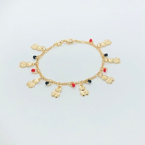 May include: Gold-toned charm bracelet featuring bear-shaped charms and small red and black beads. The bracelet is on a white background. The bracelet has a delicate chain and a lobster clasp closure.