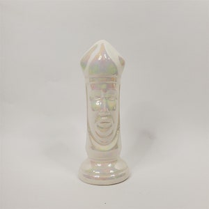 May include: White ceramic figurine of a person wearing a hat. The figurine has a detailed face and is iridescent.