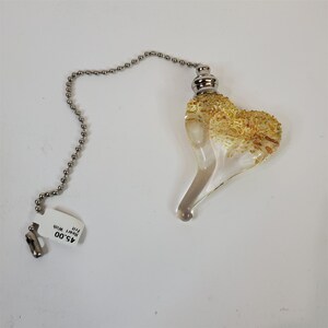 Könnte beinhalten: Ein durchsichtiger, herzförmiger Lüfterzug aus Glas mit goldenen Flocken und einer silbernen Kette. Das Etikett lautet "A5.00 Heart with Pull"