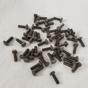 May include: A large quantity of silver-toned metal T-nuts. The T-nuts are scattered on a white surface.