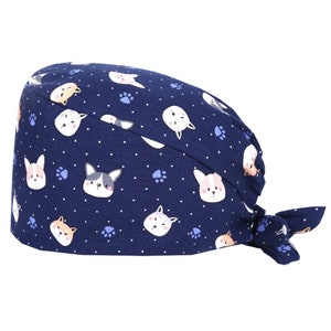 May include: A navy blue surgical scrub hat with a pattern of white paw prints and cartoon dogs. The hat has a tie at the back.