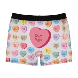 May include: White boxer shorts with a pink and white candy heart pattern. The hearts have various sayings on them, including "Cute Tush" and "Hey Hot Schliff".