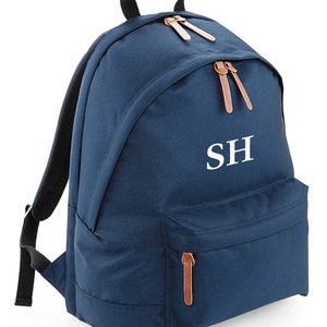 May include: A navy blue backpack with brown leather accents and a white embroidered monogram "SH".