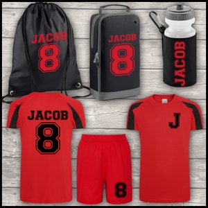 May include: Red and black football kit set with a black drawstring bag, a black and grey shoe bag, and a white water bottle with a black sleeve. The kit includes a red jersey with black sleeves and black trim, red shorts with black trim, and a black water bottle sleeve with the name "Jacob" and the number "8" printed on it. The bag and shoe bag also have the name "Jacob" and the number "8" printed on them.