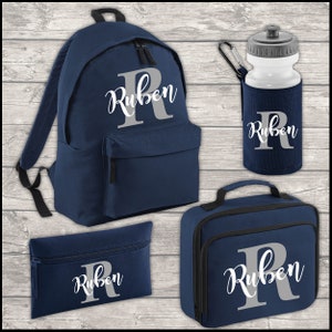 May include: A navy blue personalised school set with the name "Ruben" in white lettering on a grey background. The set includes a backpack, lunch bag, pencil case and water bottle.