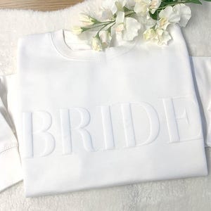 May include: White sweatshirt with the word "BRIDE" embossed in raised lettering.