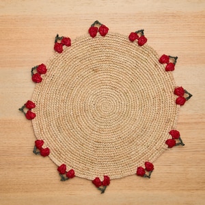 May include: A round, beige crocheted placemat with a red cherry design around the edge.
