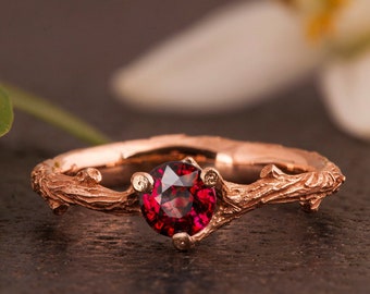 May include: A rose gold ring with a red gemstone set in a twig-like band.