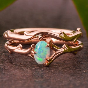 May include: A rose gold ring set with a delicate branch design and a white opal gemstone.