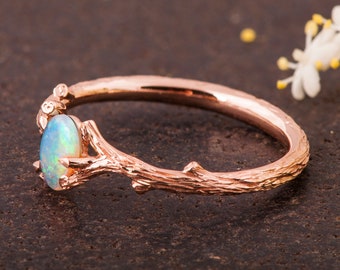 May include: A delicate rose gold ring with a branch design and a light blue opal gemstone.