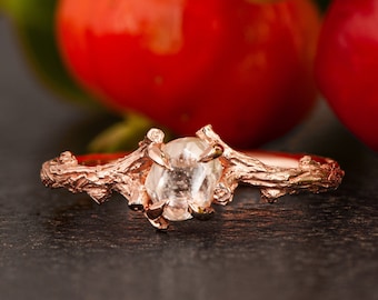 May include: A rose gold ring featuring a clear, oval-shaped gemstone set in a branch-like design.