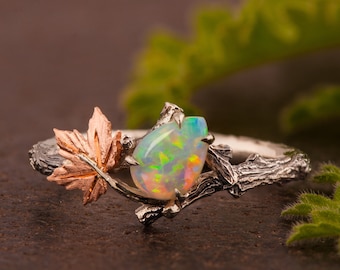 May include: A sterling silver ring featuring a pear-shaped opal gemstone with vibrant colors. The ring has a nature-inspired design with a rose gold maple leaf and branch detailing. The opal is set in a prong setting, and the band has a textured finish.