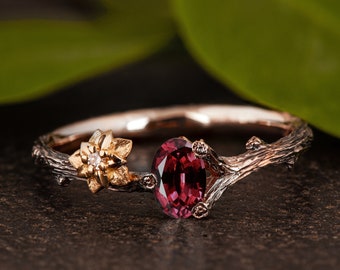May include: A delicate ring with a twig design, featuring a red oval gemstone and a small flower with a diamond accent.
