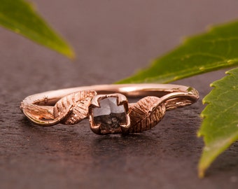 May include: A rose gold ring with a black diamond set in a leaf design.