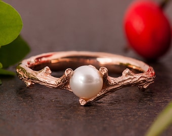 May include: A rose gold ring featuring a delicate twig design with a single white pearl at its centre.