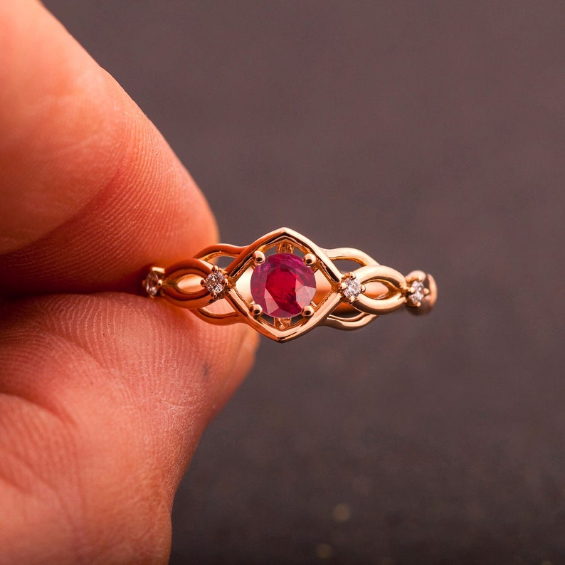 May include: A gold ring with a red ruby gemstone and smaller diamonds set in a delicate, interwoven band.
