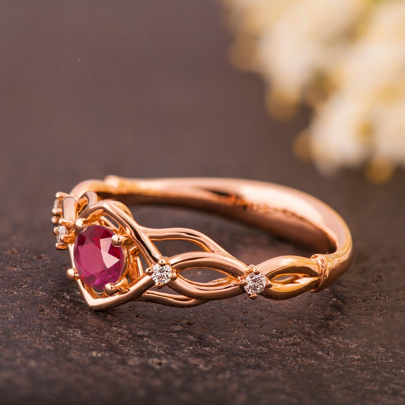 May include: A rose gold engagement ring with a ruby center stone and diamond accents. The ring features a delicate, intertwined design.