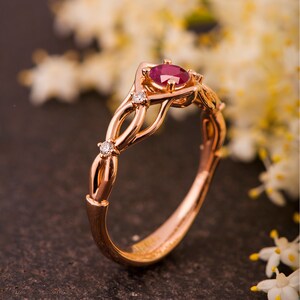 May include: A rose gold engagement ring with a ruby center stone and small diamonds on the band. The ring has a delicate, intertwined design.