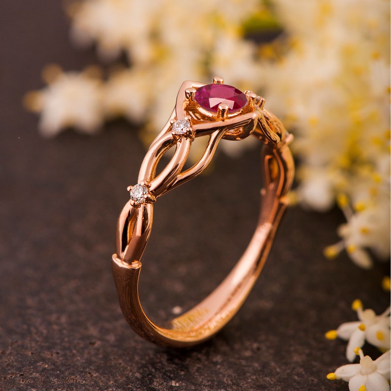 May include: A rose gold engagement ring with a ruby center stone and small diamonds on the band. The ring has a delicate, intertwined design.
