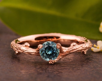 May include: A rose gold ring with a blue gemstone set in a branch-like band.
