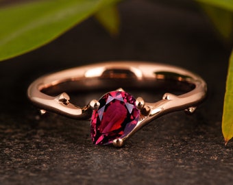 May include: A rose gold ring with a pear-shaped red gemstone set in a branch-like band.