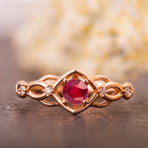 May include: A rose gold ring with a ruby gemstone surrounded by a delicate, intricate design of smaller diamonds.