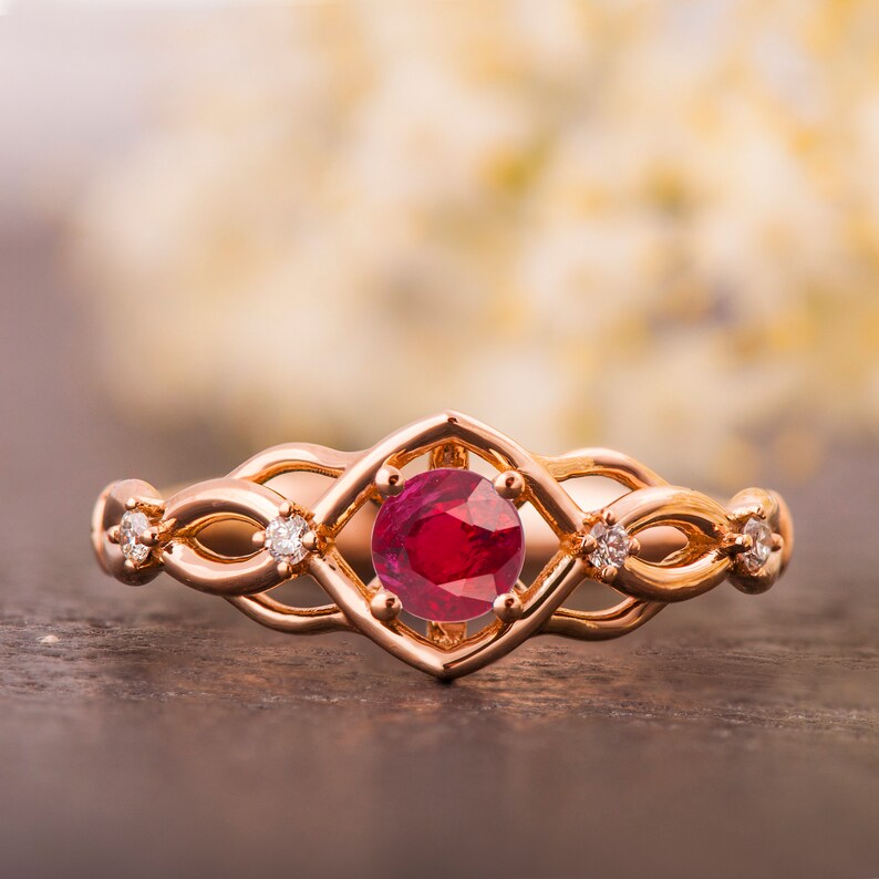 May include: A rose gold ring with a ruby gemstone surrounded by a delicate, intricate design of smaller diamonds.