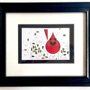 May include: Framed art print of a stylised red cardinal. The artwork has a minimalist design with a white background, black frame, and a white mount. The cardinal is depicted with geometric shapes and lines.