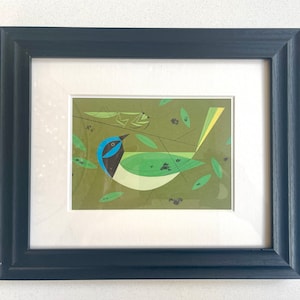 Puede incluir: Lámina artística enmarcada que representa un pájaro estilizado con plumaje azul, negro y verde, posado en una rama con hojas. La obra de arte tiene una estética moderna de mediados de siglo, sobre un fondo verde apagado. El marco es azul marino oscuro.