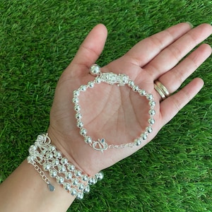 May include: A silver bracelet with a dragon charm and a bell. The bracelet is made of small silver beads and has a clasp closure.