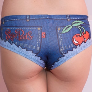 Pu&ograve; includere: Intimo in denim blu con un aspetto consumato e una tasca con il testo "Sugar Pants" e una grafica di una ciliegia.