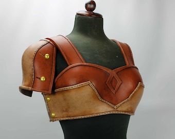 May include: A brown leather armour chest piece with gold accents and stitching. The armour is on a black mannequin.