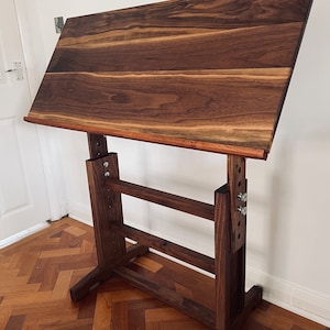 May include: A dark brown wooden drafting table with adjustable height. The table has a large rectangular top and a sturdy base with multiple adjustable legs.