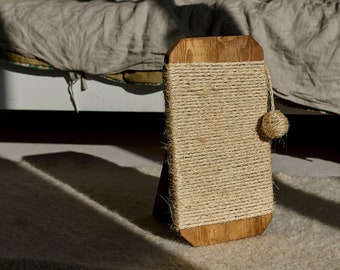 May include: A rectangular wooden scratching post featuring a natural wood frame wrapped in thick, light tan sisal rope. A small, round sisal ball toy hangs from a short string attached to the side of the post, which stands upright on a base.