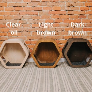 May include: Three hexagonal wooden pet beds in clear oil, light brown, and dark brown finishes. Each bed has a dark gray interior and is displayed against a brick wall. The text "Clear oil", "Light brown", and "Dark brown" is above each bed.